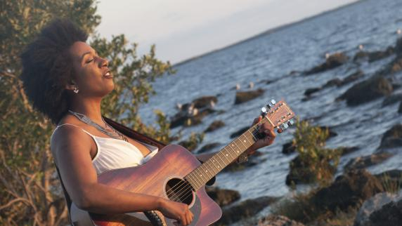 Image d&eacute;corative d'une chanteuse jouant de la guitare face &agrave; la mer